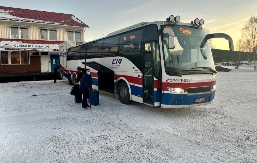 En buss mot Pajala vid Överkalix busstation en vintermorgon. Två resenärer stiger på i snön.