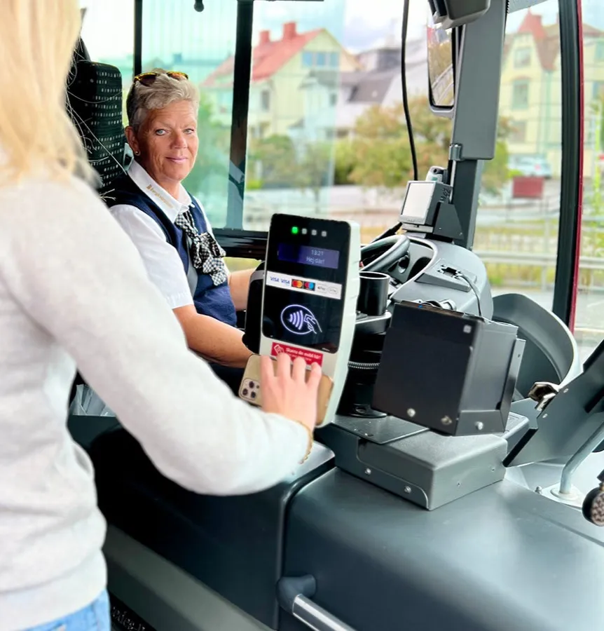 En resenär håller sitt färdbevis mot viseringsutrustningen vid förarplatsen i en buss.