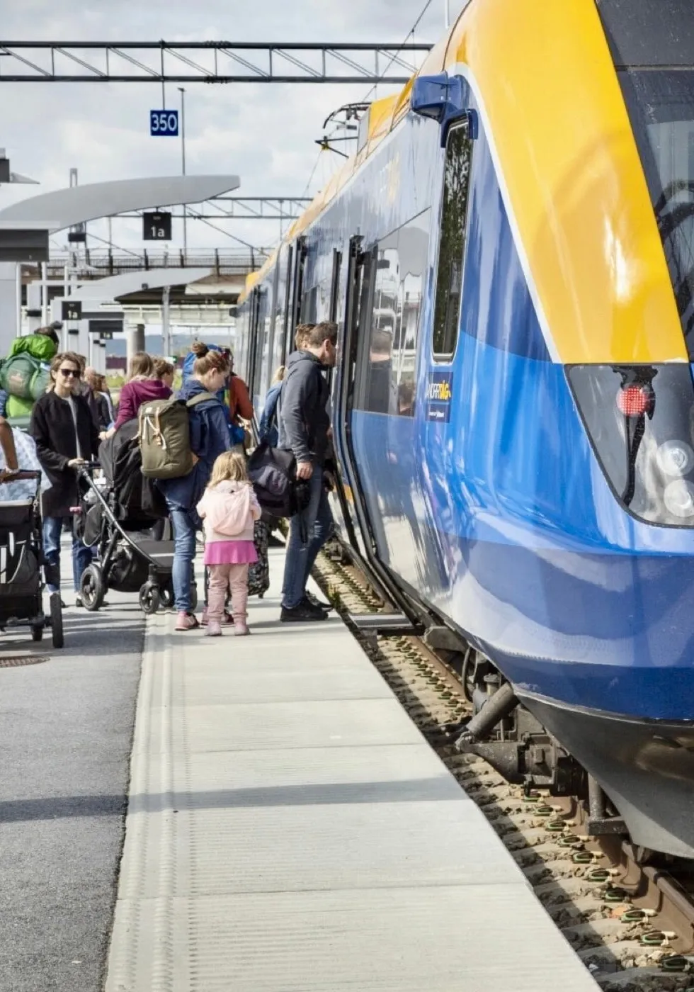 En familj med barnvagn stiger på ett regionaltåg vid en perrong.